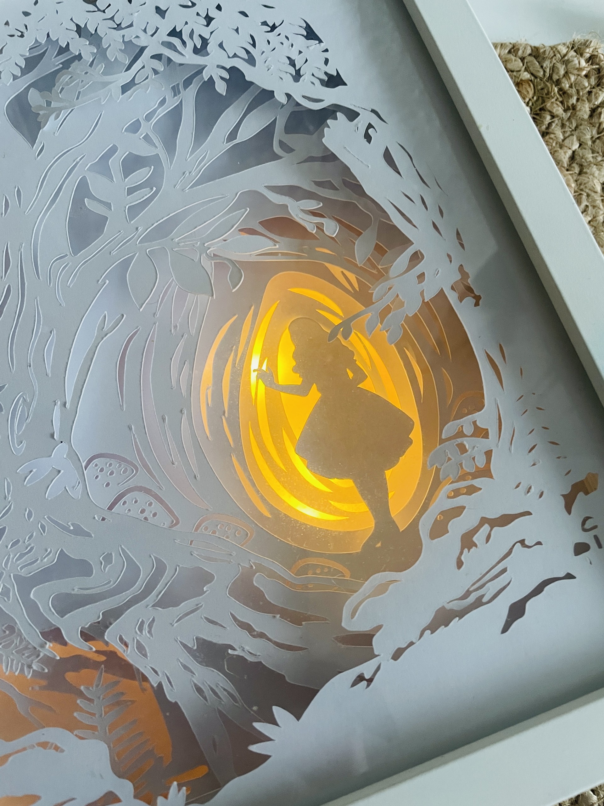 Käsitööna valmistatud 3D paberilõikega LED valguskast valges puitraamis, kujutades muinasjutulist metsa sooja valgusega